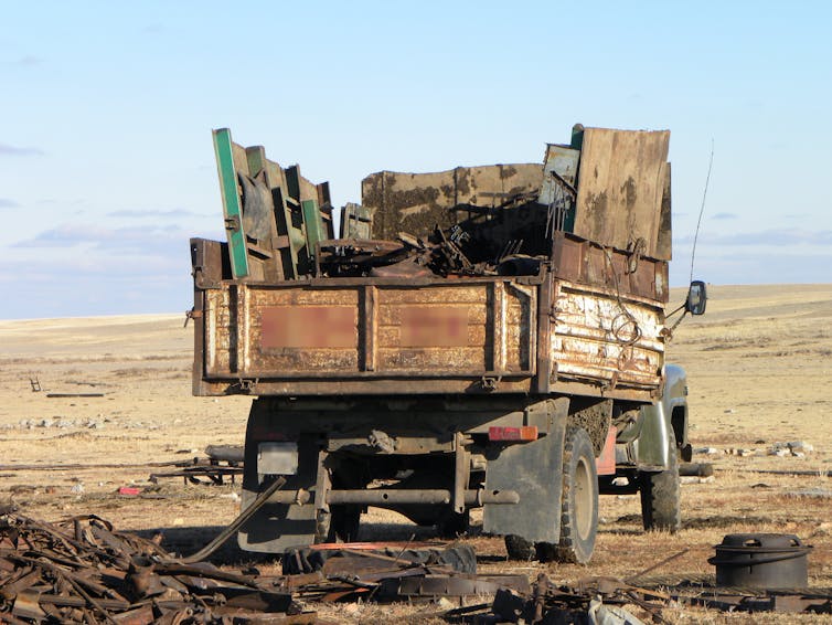 truck with metal piled in back parked on open landscape, salvaged metal is on the ground around it