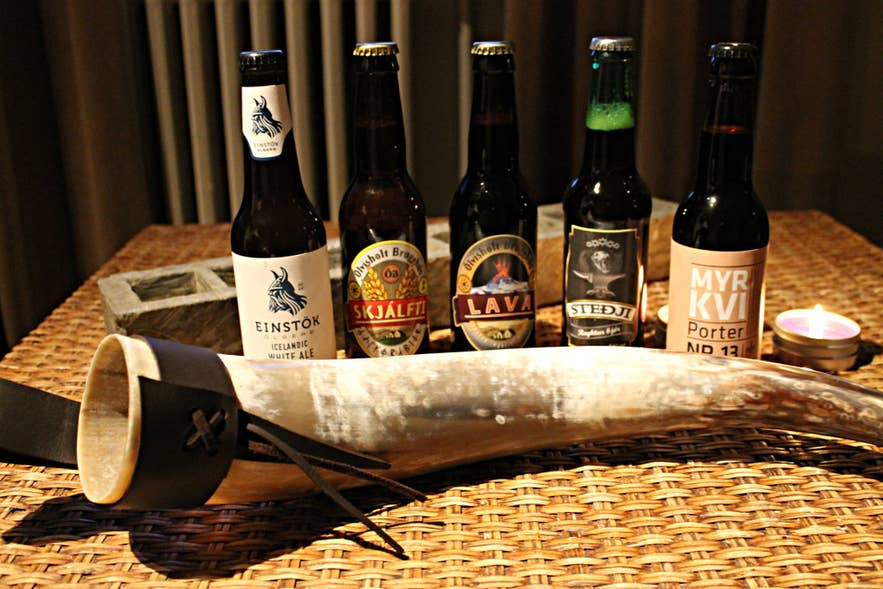 Several bottles of Icelandic beer and a drinking horn displayed on a straw table. Several bottles of Icelandic beer and a drinking horn displayed on a straw table.