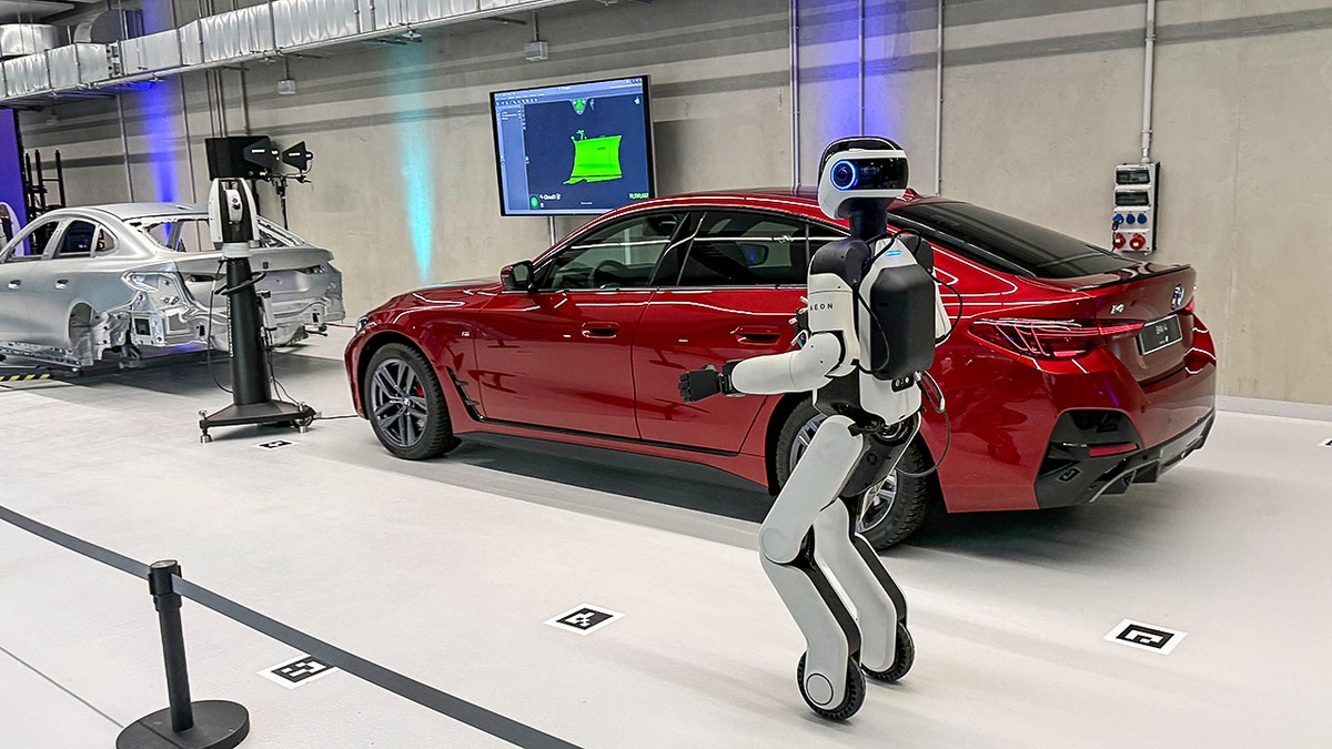 A humanoid robot in front of a red car.