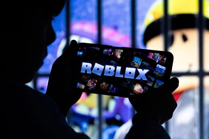 A boy poses for a photo while holding a smartphone in front of a screen displaying a character of the U.S. childrens video game Roblox, in this illustration taken December 8, 2025. Photo by Reuters