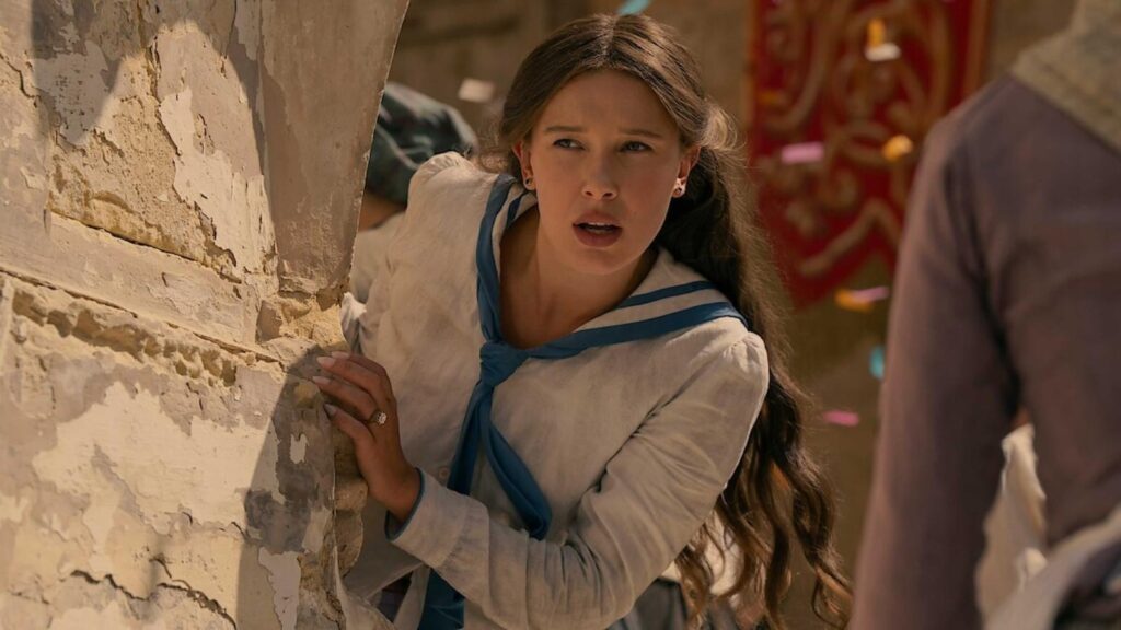 Millie Bobby Brown as Enola Holmes looking alert beside wall in Enola Holmes 3