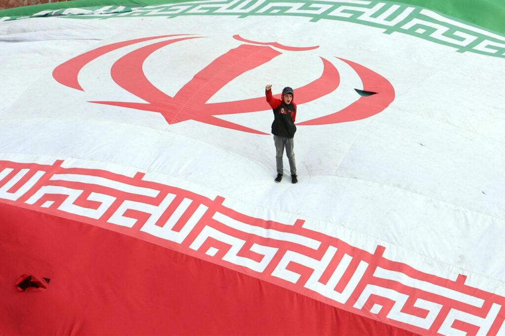 A boy raises his fist while standing on a giant Iranian flag during the funeral of Alireza Tangsiri, commander of the Iranian Revolutionary Guards