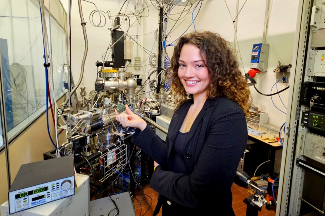 Jenna Woods wearing a black blazer posing with complex lab machinery. 