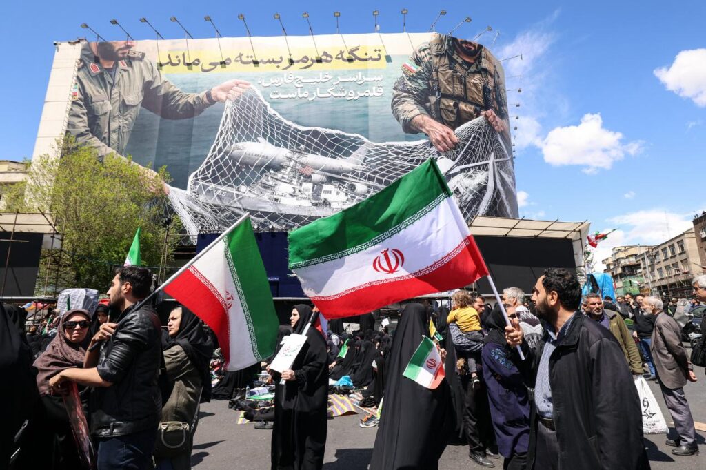 Iranians hold national flags beneath a large billboard reading