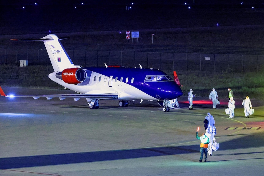 A plane on the tarmac at the airport surrounded by people in white body suits carrying white bags.