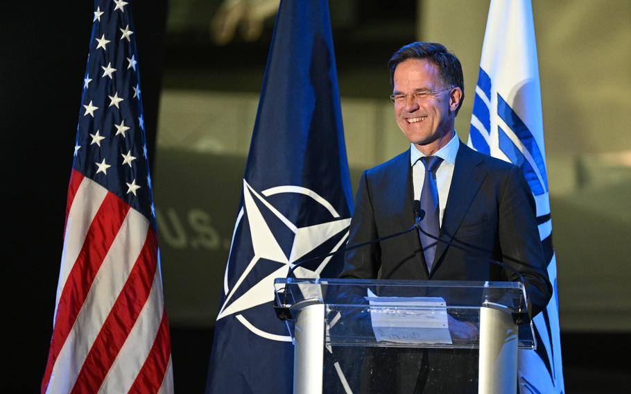 Man speaks at a podium with U.S. and NATO flags behind him.