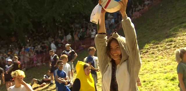 Alix is holding up her roll of cheese and is grinning.