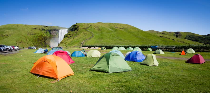 Colorful tents set up near Skogafoss Waterfall on a sunny day, one of the best ways to see Iceland's nature up close. Colorful tents set up near Skogafoss Waterfall on a sunny day, one of the best ways to see Iceland's nature up close.