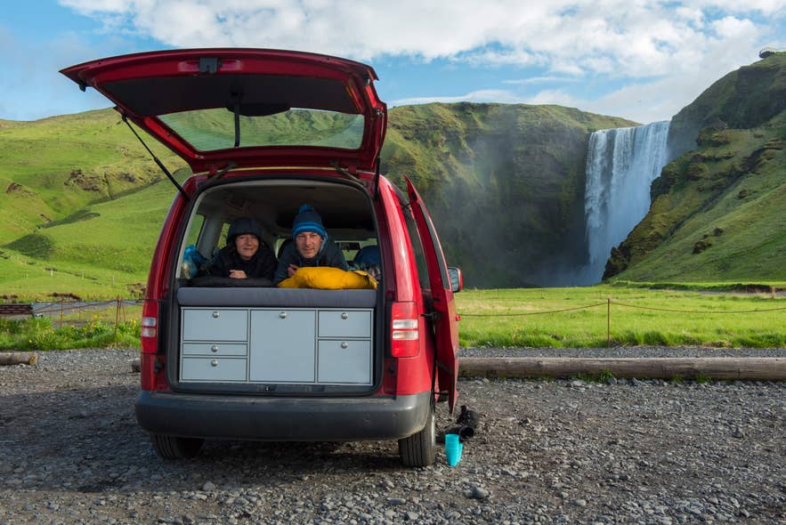 A couple relaxing in a campervan during a scenic camping trip, with Skogafoss Waterfall in the background. A couple relaxing in a campervan during a scenic camping trip, with Skogafoss Waterfall in the background.