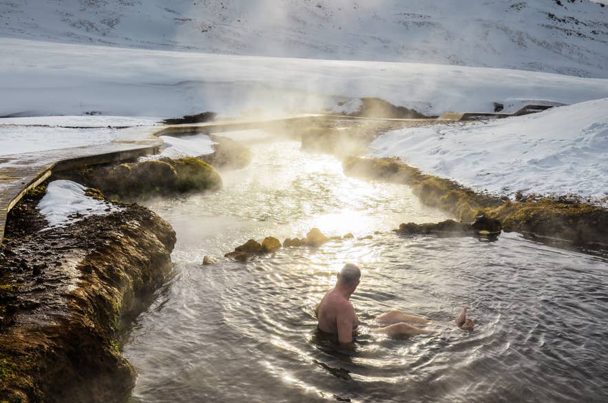 Man bathing in a steaming hot spring surrounded by snow in Reykjadalur Valley, a popular geothermal spot in Iceland. Man bathing in a steaming hot spring surrounded by snow in Reykjadalur Valley, a popular geothermal spot in Iceland.