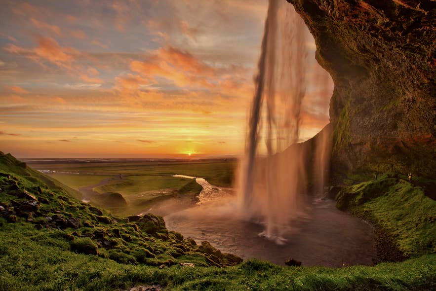 Seljalandsfoss waterfall glowing under the midnight sun in Iceland, with golden skies and lush green hills. Seljalandsfoss waterfall glowing under the midnight sun in Iceland, with golden skies and lush green hills.
