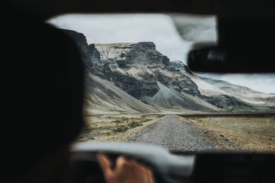 Driving on a remote gravel road toward rugged mountains, perfect for vacationing in Iceland. Driving on a remote gravel road toward rugged mountains, perfect for vacationing in Iceland.