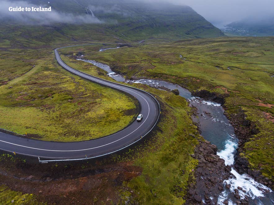Scenic winding road through green Icelandic valley with a single car, perfect for a self-drive in Iceland adventure. Scenic winding road through green Icelandic valley with a single car, perfect for a self-drive in Iceland adventure.