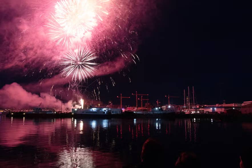 Fireworks light up the night sky above Reykjavik Harbor, reflecting on calm waters during Iceland’s New Year’s Eve celebrations.
