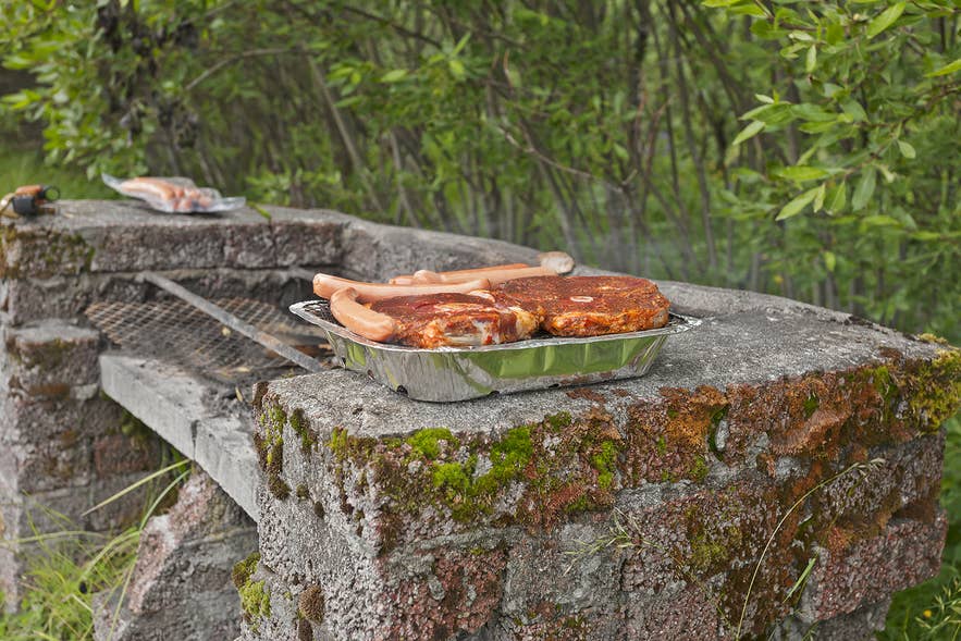 Icelanders grill marinated meat and sausages on outdoor barbecue in Icelandic nature. Icelanders grill marinated meat and sausages on outdoor barbecue in Icelandic nature.