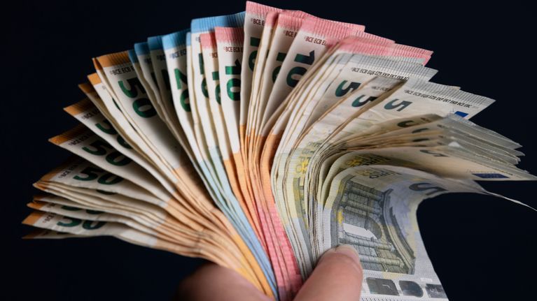 Hand holding a large pile of euro banknotes.