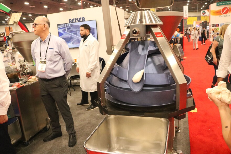 A metal and rubber machine pushes out a dough ball in a large expo center.