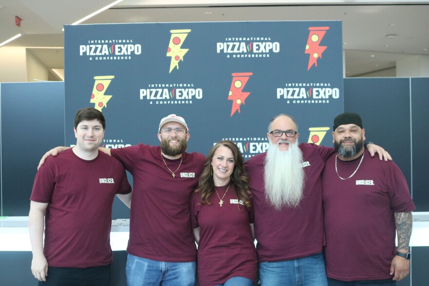 Five people wearing matching shirts in front of an International Pizza Expo sign.