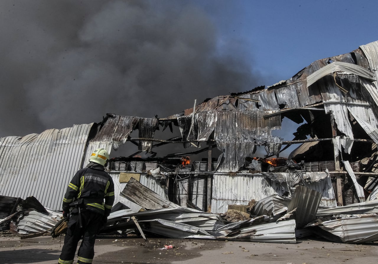 A helmeted and uniformed firefighter with his back to the camera is shown in front of a hulking piece of metal and black smoke.