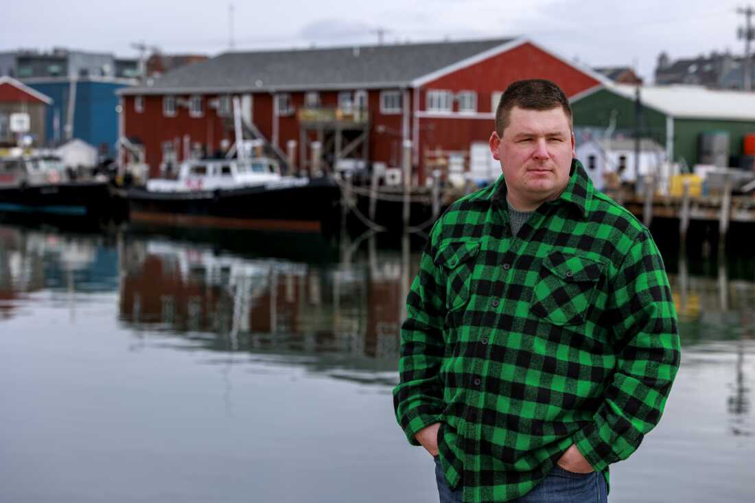 Fisherman Devyn Campbell stands near the water outside the Portland Fish Exchange. Boats and a marina are behind him.