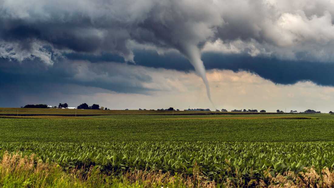 A landscape with farmlands, grey clouds, and a tornado approaching.