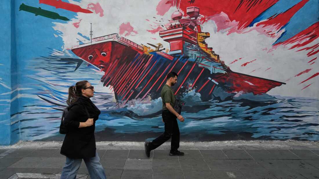 People walk past a mural depicting a U.S. aircraft carrier under missile attack by Iran in downtown Tehran, on May 17. The two countries agreed to a ceasefire but strikes have continued including U.S. military strikes against Iranian targets on Monday.