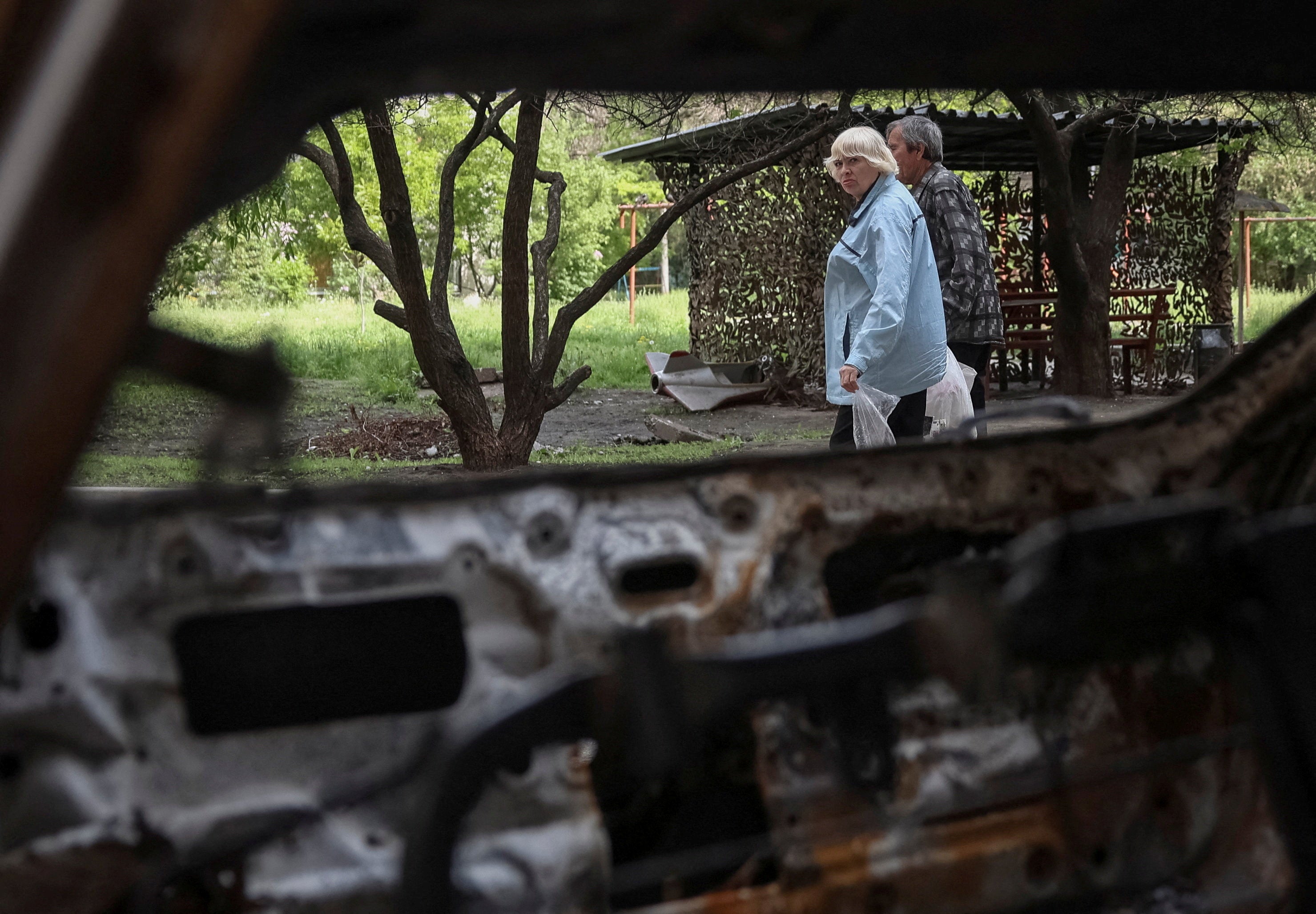 Residents walk near a destroyed car amid Russia's attack on Ukraine in the frontline town of Druzhkivka in Donetsk region