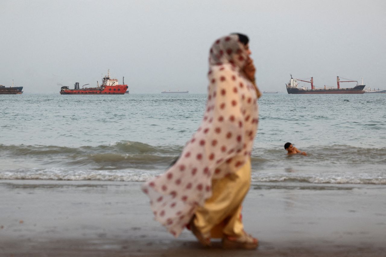 People walk on the beach, with vessels in the Strait of Hormuz visible near the beach of Bandar Abbas, Iran, on May 22.