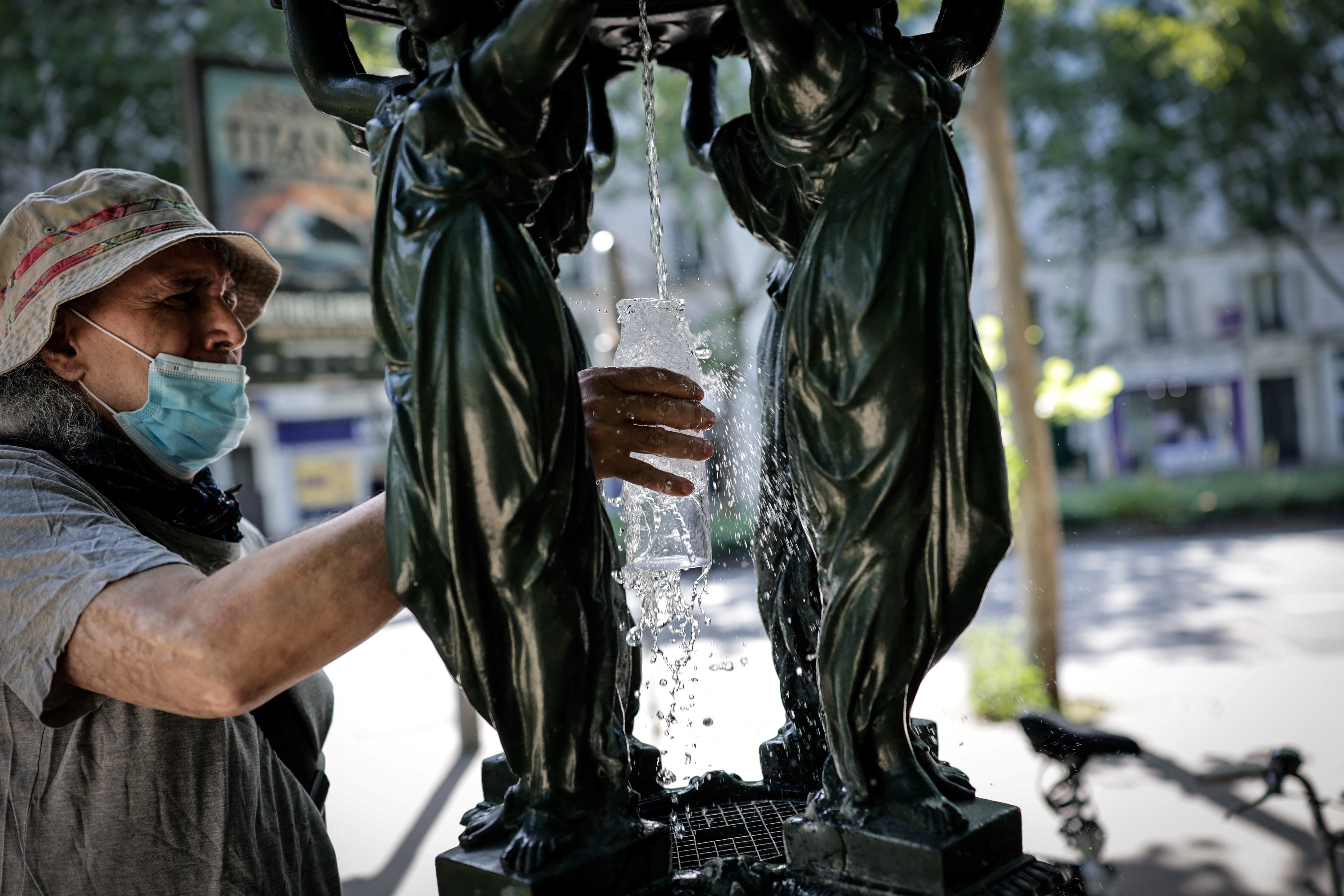 A man fills a glass of water at a public fountain in the Montparnasse district of Paris on May 25
