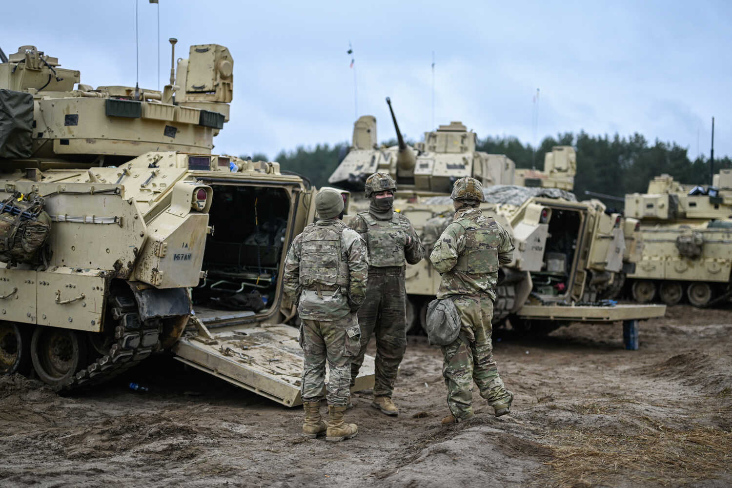 Soldiers in camouflage near the open rear of a pale armored vehicle standing on mud.