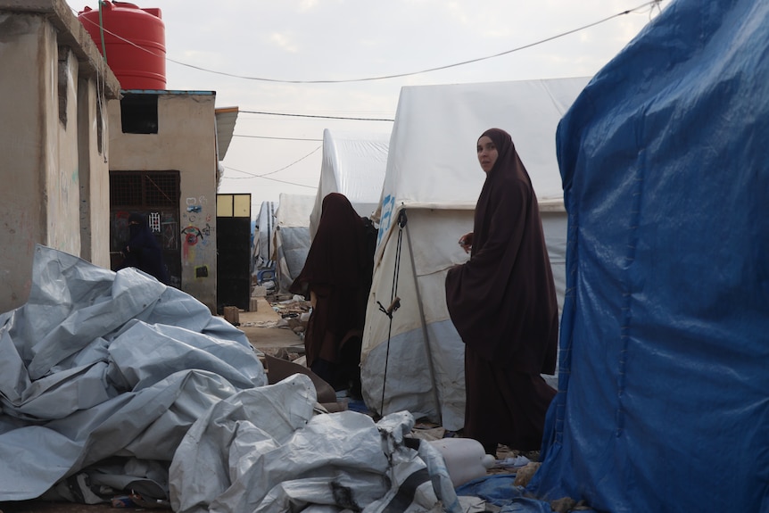 Two women in a burkas walking through a densely-populated camp.