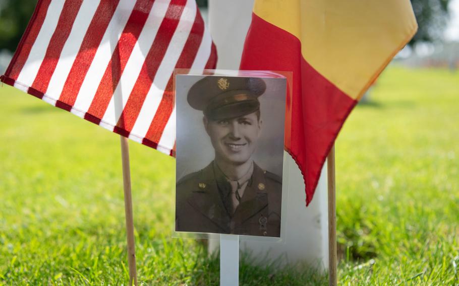 A photograph of Army Pfc. Dee L. Martin, who was killed on Dec. 21, 1944, stands next to his grave at Henri-Chapelle American Cemetery, along with a U.S. and Belgian flag on May 23, 2026.