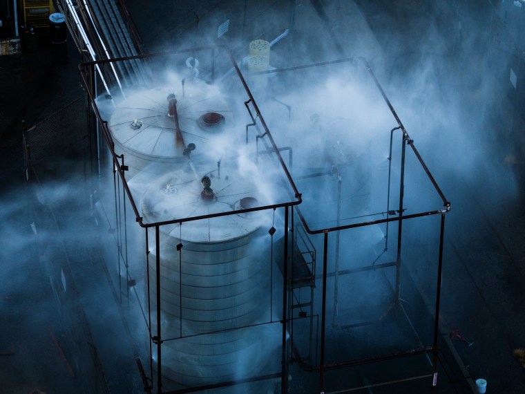 Spraying water and mist on a large chemical tank at dusk.