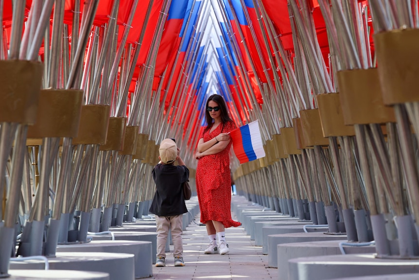 A woman holding a Russian flag and young child standing in a large memorial featuring Russian flags.