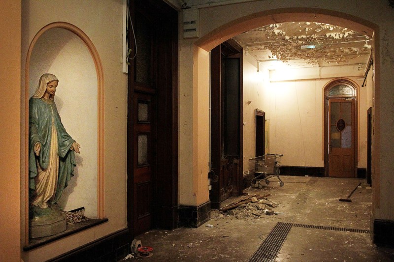 A dilapidated interior corridor of a building that includes a statue of the Virgin Mary.
