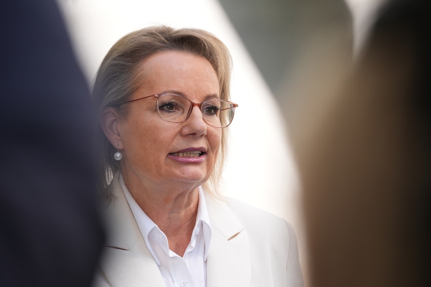 A woman with dark blonde hair, wearing glasses.