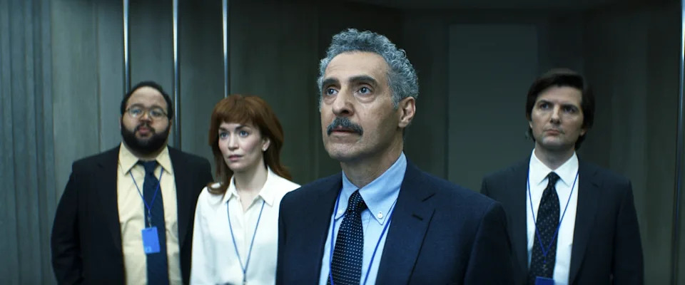 Group of four people in business attire looking ahead seriously, suggesting a tense scene in a TV show or movie