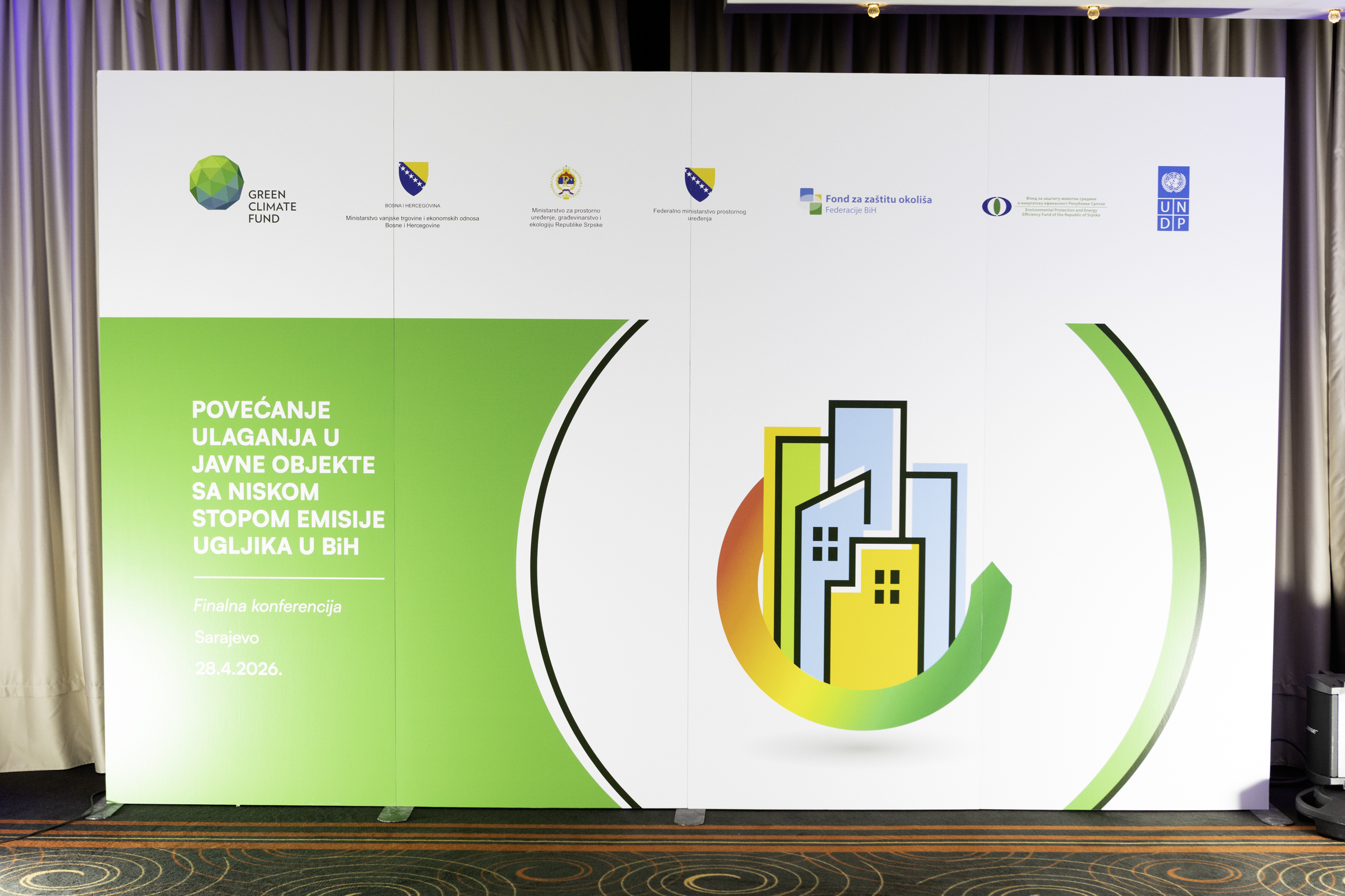Stage backdrop with a green panel and a circular city skyline graphic; sponsor logos at top.