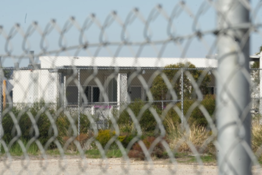 A building with a sheet-metal roof, as seen through a chain-link fence.