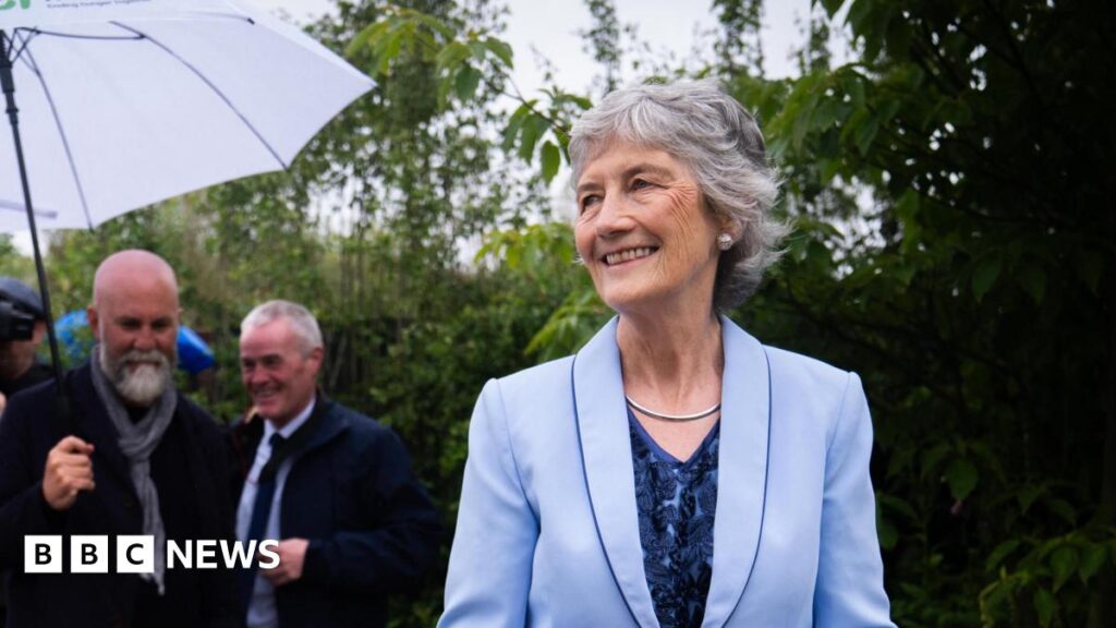 Catherine Connolly: Irish President visits Chelsea Flower Show A woman in a blue suit and blue dress, with a navy top looks down at an out-of-focus flower bed
