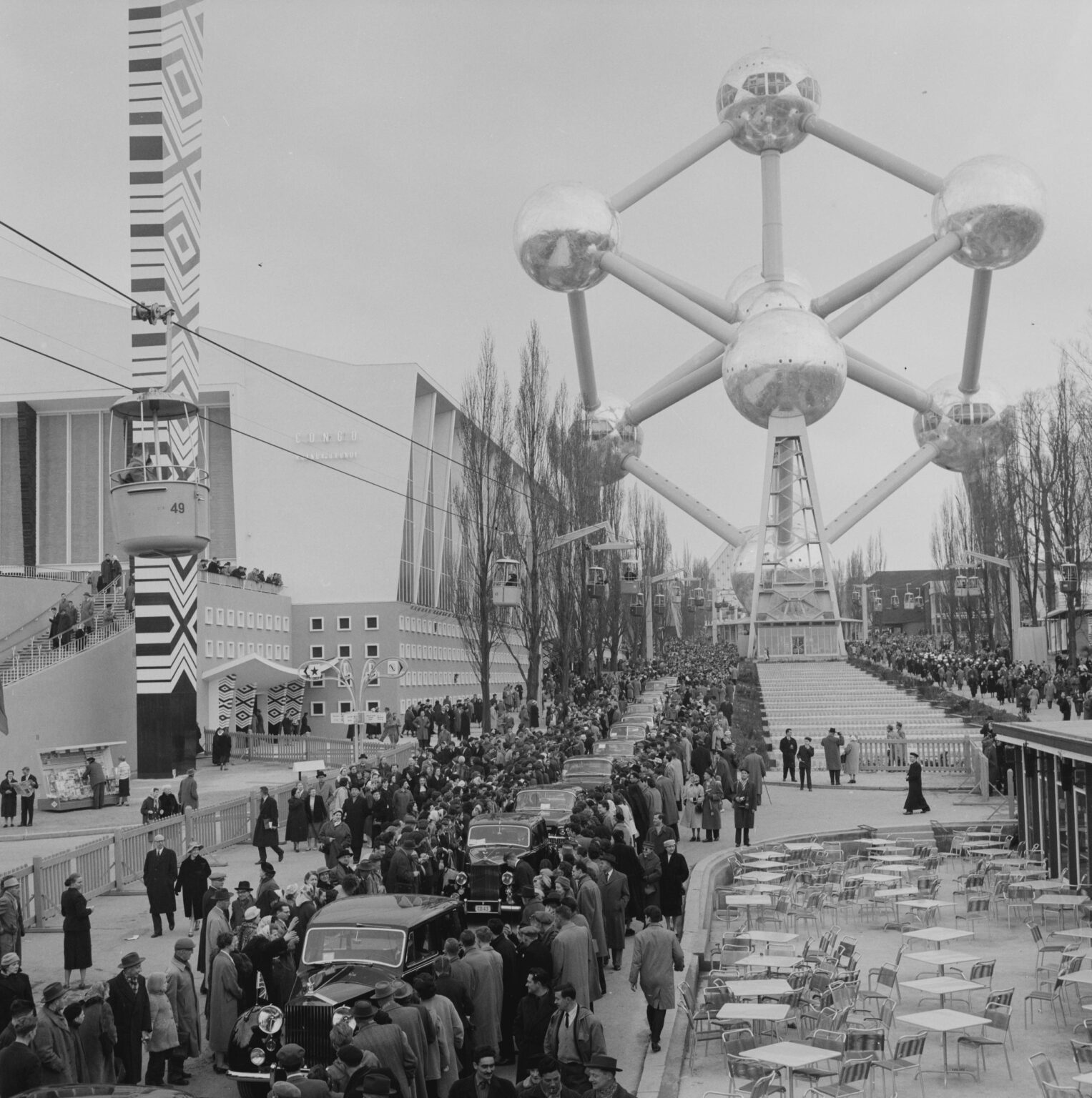 A view towards the Atomium during the opening of the 1958 Brussels World's Fair, with visitors visitors and cars queuing along the exhibition grounds.