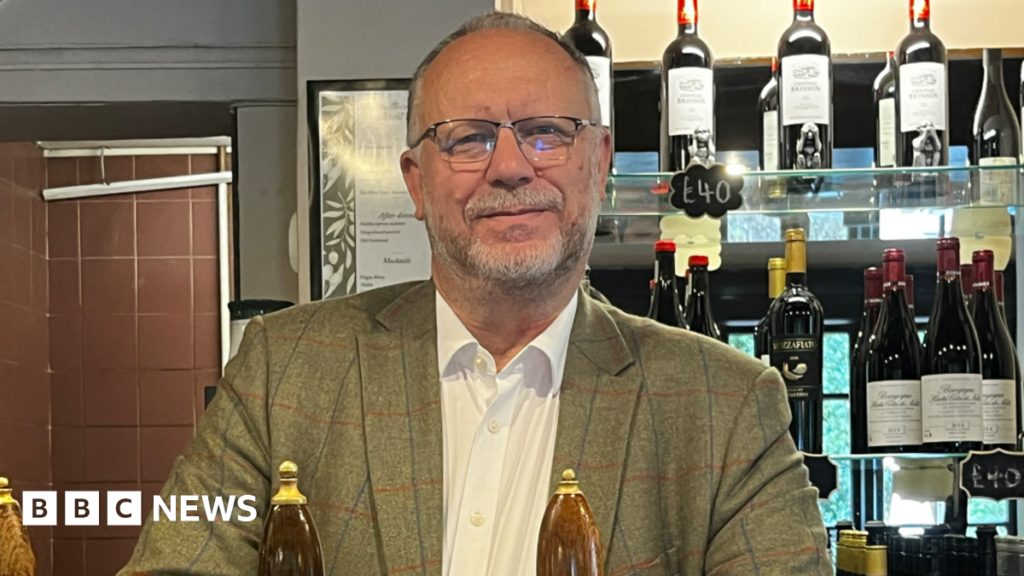Surrey pub boss hits out at UK Power Networks after blackout shuts business Pub owner Nigel Farnfield behind the bar at The Olive Tree in Sutton Green, pictured with ale pumps and a wall of wine bottles.