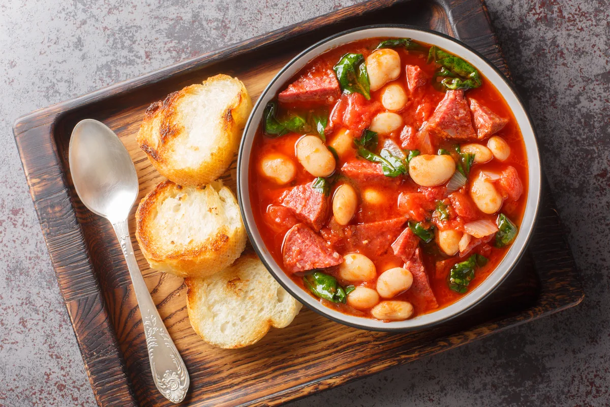 Crockpot stew with chorizo, butter bean and spinach close-up in a bowl served with toasted bread on the table