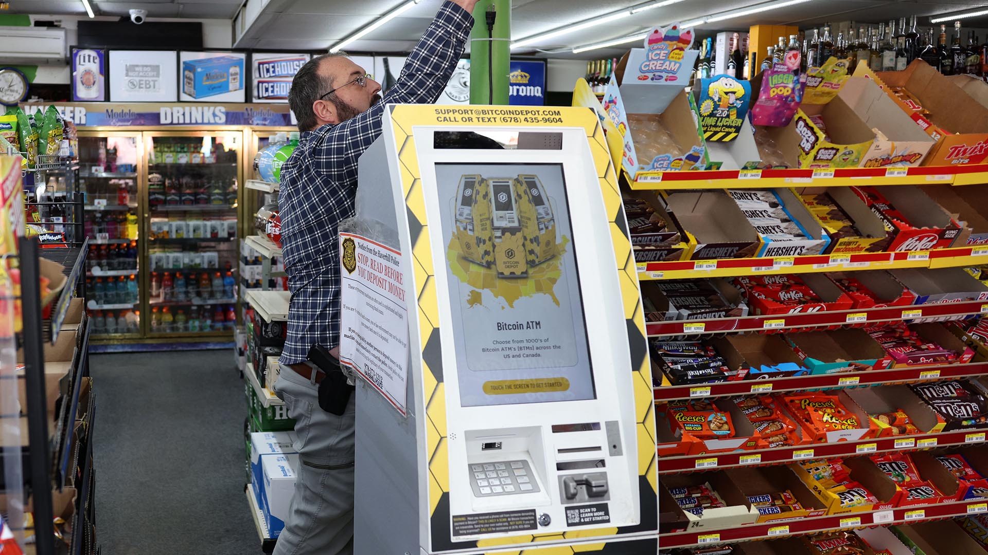 Photo of a Bitcoin Depot ATM in a convenience store with a man unplugging the machine.