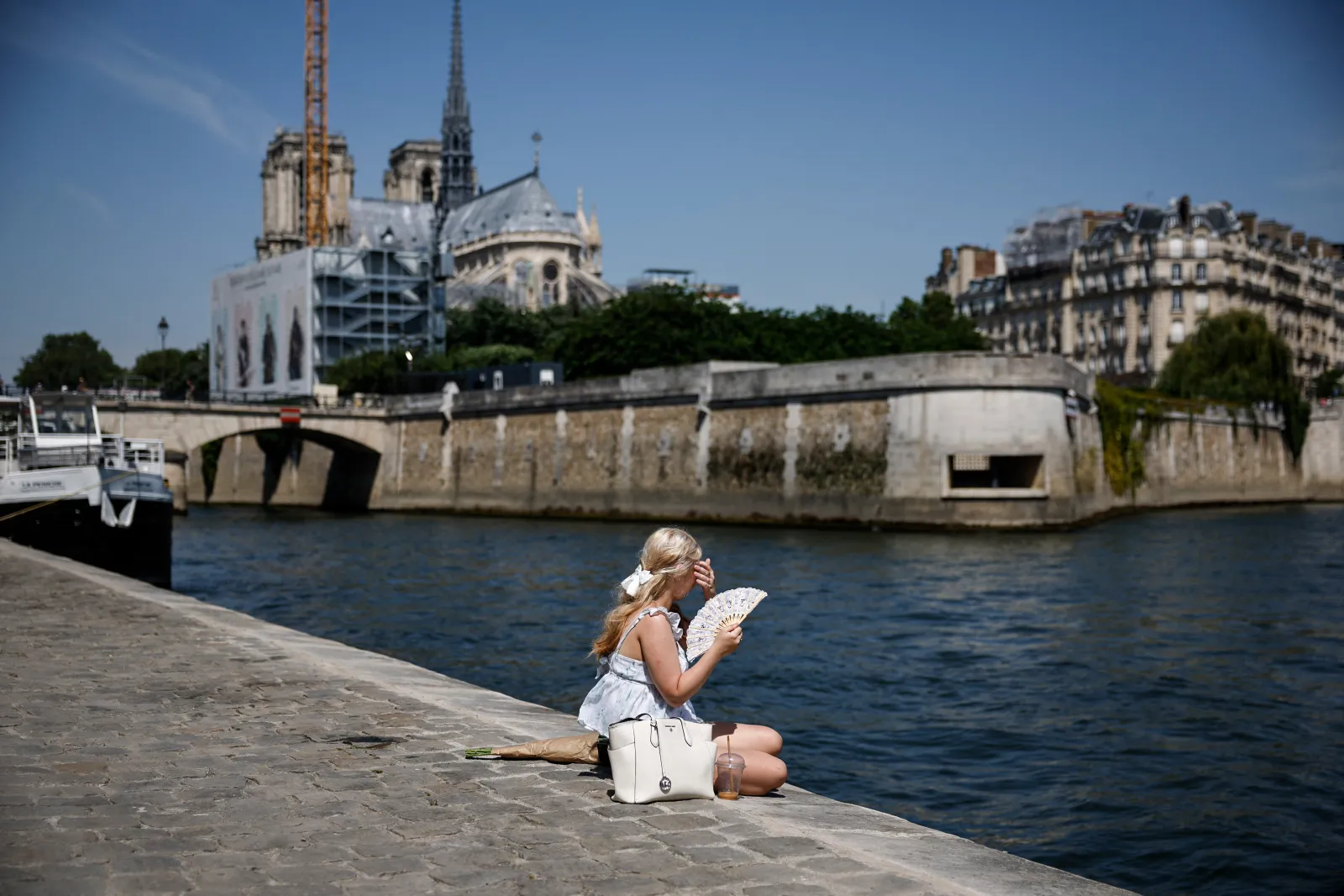 A person uses a fan as she sits on the Seine river banks behind the Notre-Dame Cathedral in Paris as a record-breaking early heatwave scorches a swathe of Western Europe on May 28, 2026.