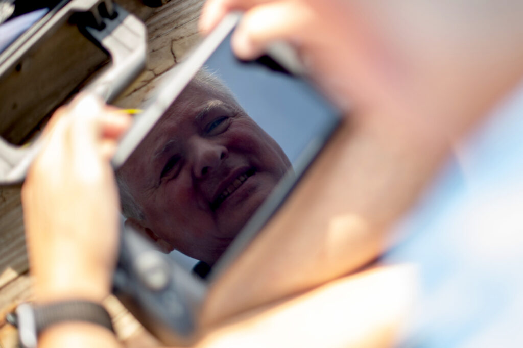 Mark Patterson, an older white man, is reflected on a screen attached to a device he is holding.