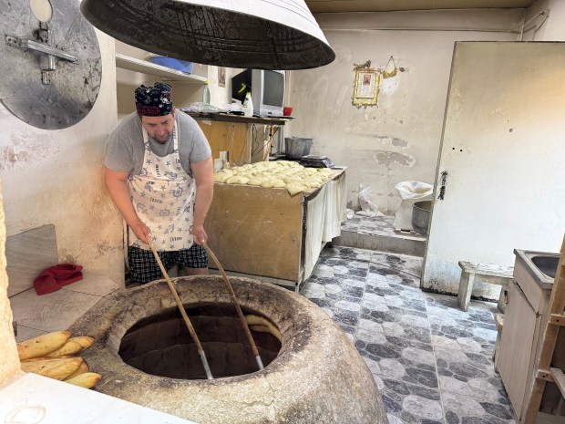 A person using long rods to position bread in a clay oven