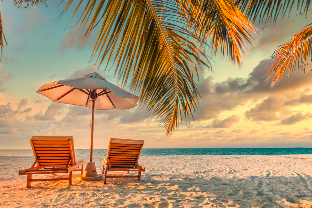 Beautiful panoramic tropical beach. Sunset summer island landscape with couple chairs umbrella palm leaves calm sea shore, coast. Romantic travel panorama honeymoon destination banner vacation holiday