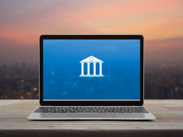 Laptop displaying a bank icon on a blue screen with a blurred city skyline in the background.