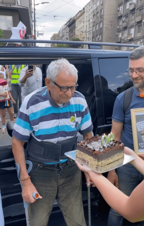 Grandpa Velimir, despite a hip injury and the surgery he had, came to the rally organized at Slavija Square. As a sign of welcome, the crowd greeted him with a birthday cake to celebrate his 90th birthday. Happy birthday to him!
